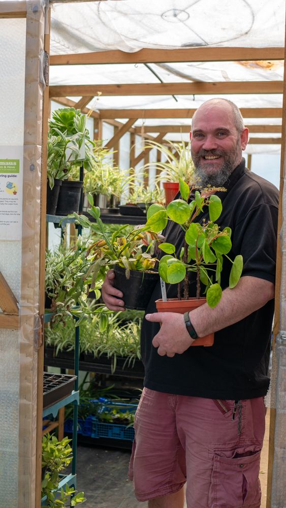 Program participant holding potted plants in a greenhouse.
